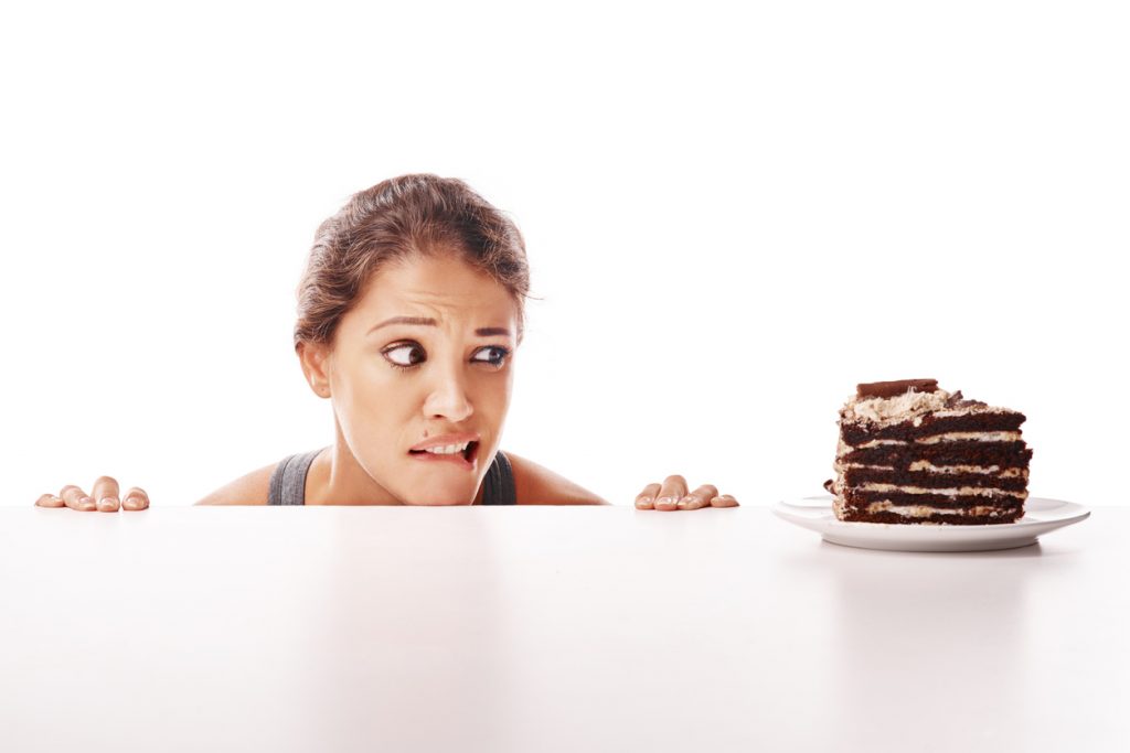 Desejo por bolo de chocolate com expressão de culpa, gesto de hesitação e tensão emocional face ao alimento