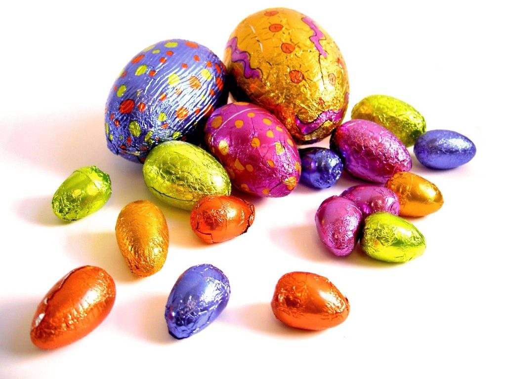 Ovos de chocolate coloridos espalhados sobre fundo branco, ideais para a Páscoa mas ricos em açúcares e gorduras