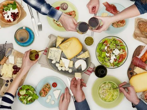 Mesa com queijos, saladas, fiambre, azeite e vinho — refeição low carb partilhada em contexto social