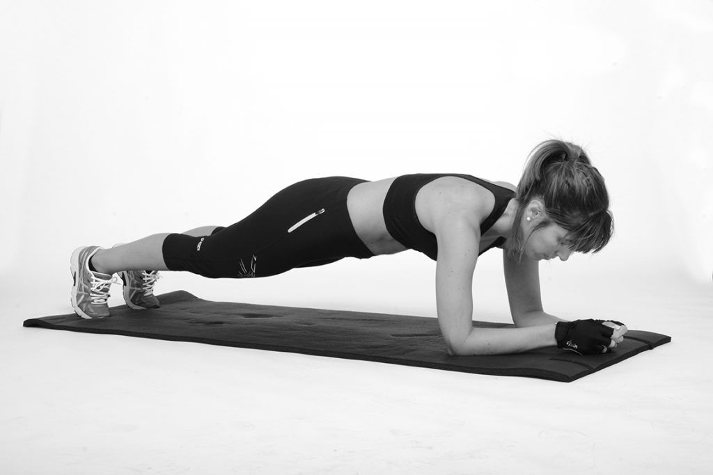 Mulher faz prancha abdominal em casa com roupa desportiva e tapete de exercício para fortalecer o core e emagrecer
