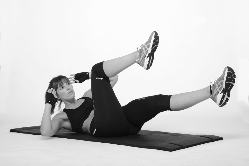 Mulher a fazer abdominais com pernas elevadas em tapete de exercício, gesto de emagrecimento em casa