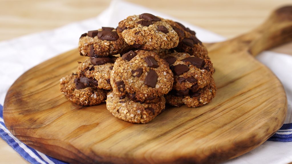 Cookies de aveia com gotas de chocolate escuro, prontos a servir num tabua de madeira rústica, ideais para um lanche