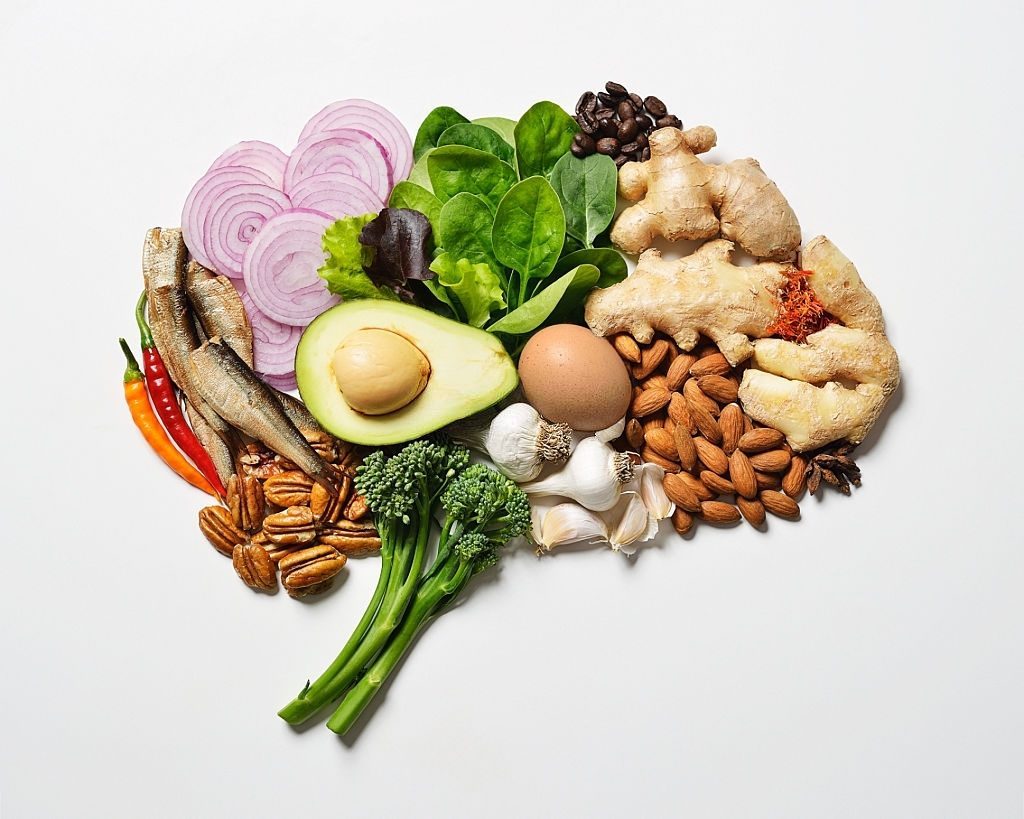 Alimentos como peixe, abacate, nozes e brócolos dispostos em forma de cérebro para ilustrar a nutrição na prevenção
