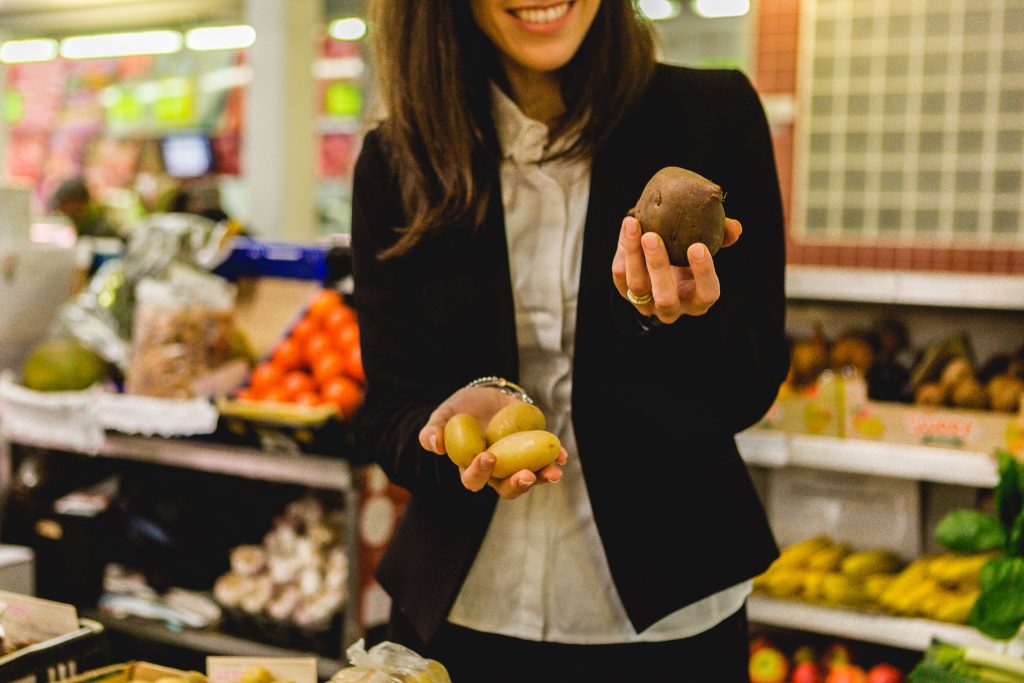 Nutricionista em supermercado escolhe batata doce e batata comum, comparando opções para planeamento alimentar